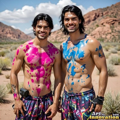 Smiling outdoors, two bare-chested men stand covered in pink and blue paint splatters