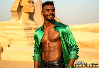 Facing forward, a happy man wearing an open green shirt stands by the Sphinx