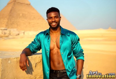 Smiling in the desert sun, a man wearing an open teal thin silk shirt leans near a pyramid