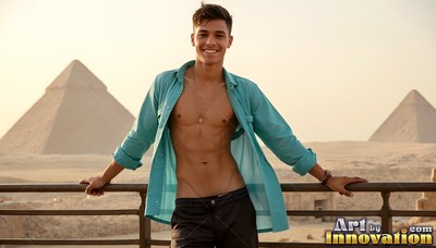 Leaning on a railing, a happy man wears an open dark teal shirt before the Giza pyramids