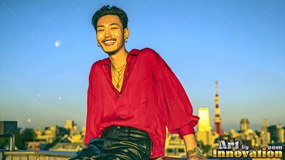 Wearing a loose red silk shirt, a smiling young man relaxes on a tokyo rooftop at sunset