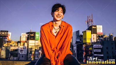 A young man in an orange shirt laughs on a Tokyo rooftop under warm late sun