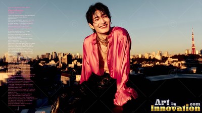 A smiling young man leans back on a rooftop in a shiny pink shirt lit by warm sunset rays