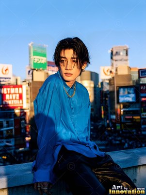 Leaning on a rooftop ledge, a young Japanese man wears a bright blue shirt at sunset