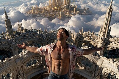 A man with an open shirt stands on a balcony above the clouds