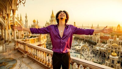 Arms spread wide, a happy man in a purple smooth silk shirt waits on a balcony at sunset