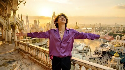A cheerful man spreads his arms on a balcony in warm sunset light