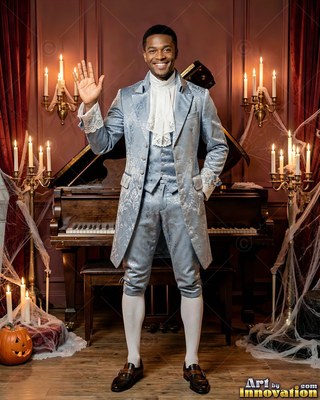 Waving near a piano, a man with a smile stands in a light blue colonial suit