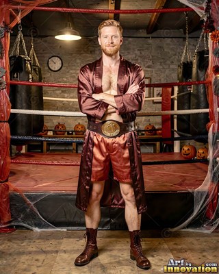 Standing arms crossed by a boxing ring, a smiling man is wearing an open satin robe