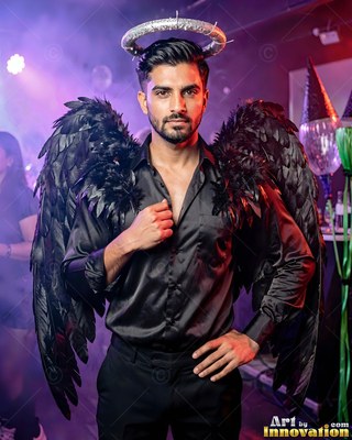 A man poses in a black fallen angel costume with feathered wings and a halo