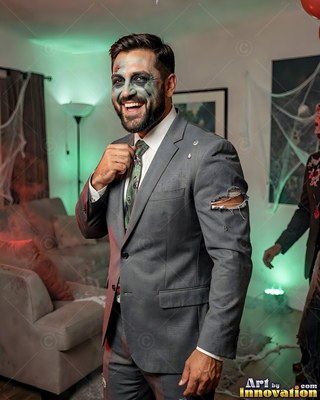 In a decorated room, a happy man sports zombie makeup and a torn gray suit