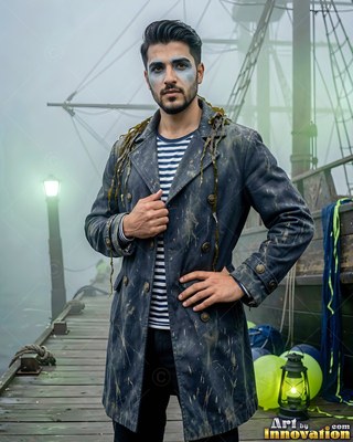 Seaweed hangs from the coat of a man in pirate makeup standing on a foggy dock