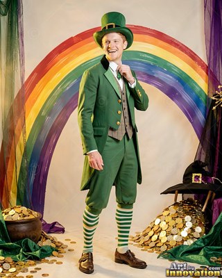 Standing in front of a painted rainbow, a smiling man is dressed in a green leprechaun suit