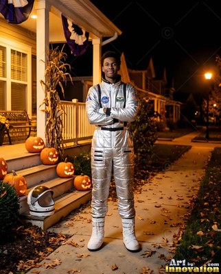 Standing on a leaf-strewn walkway, a man is dressed in a silver astronaut suit beside carved pumpkins