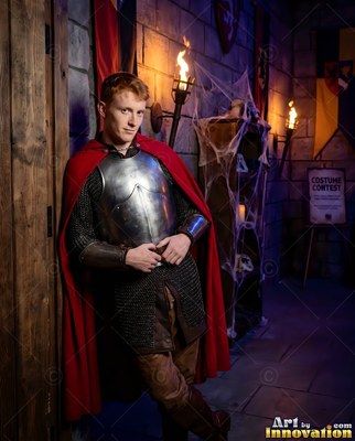 Leaning against a doorway in a stone hall, a man sports armor and a red cape