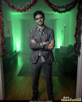 Standing with crossed arms, a man in a tattered gray suit poses under green light