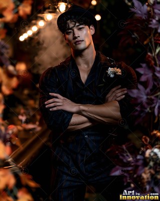 A black fedora tops a muscular man in a dark suit standing among autumn leaves