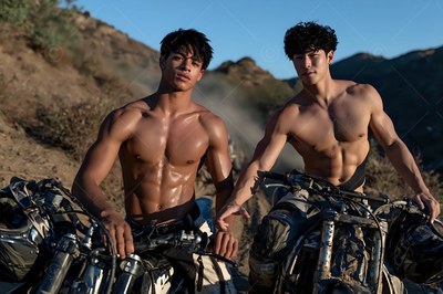 Bare-chested under a blue sky, two muscular men sit on dusty dirt bikes in the hills