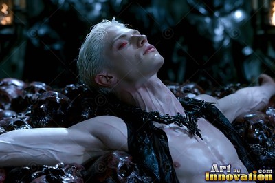 A pale man with short blond hair and red eyes lies back on a dark bed of skulls