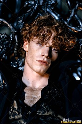 In a dark high seat, a curly-haired white-skinned man reclines in an open black shirt