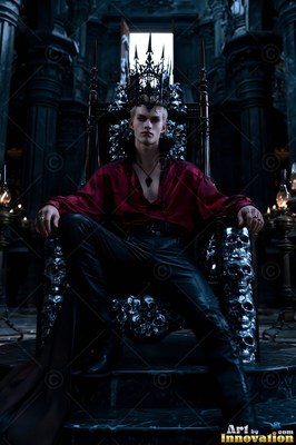 Sitting on a skull throne, a crowned man in a red shirt stares forward in a dark hall