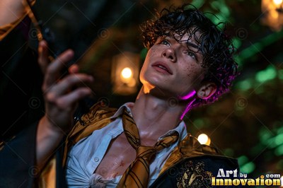 Looking up from below, a young man wears a loose gold tie in the dark woods