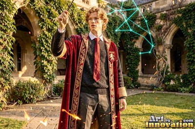 In a stone courtyard, a blond young man in a red robe raises his wand