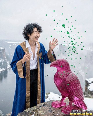 Wearing a blue robe, a smiling man stands by a pink crystal raven on a snowy cliff