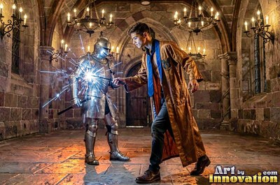 Brown robe worn by a young man pointing a wand with bright sparks at an armored knight in a stone hall