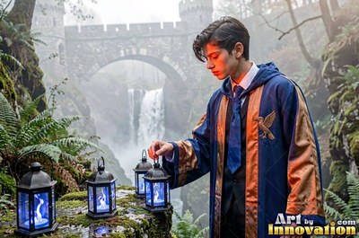 A young man in blue robes lights dark lanterns that shine blue by a waterfall bridge