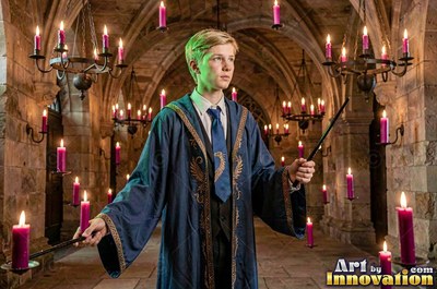 Standing in a stone hall, a young blond man holds a wand in blue robes