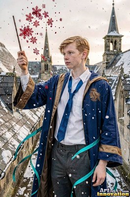 A young man raises a wand on a snowy castle rooftop beside red flakes