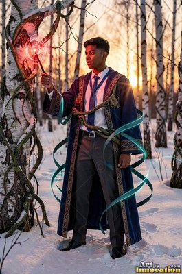 In a snowy birch forest, a young man in a blue robe points a wand at a tree trunk