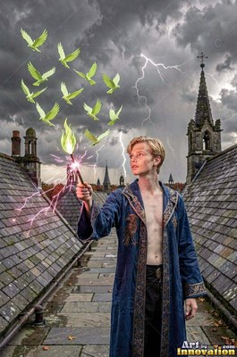 Standing on a stone roof, a blond man holds up a wand releasing green birds