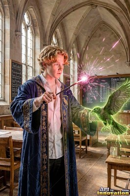In a blue velvet robe, a red-haired young man points a wand in a classroom to summon a green bird