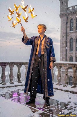 Holding flaming golden birds, a blond man in a pale blue robe stands on a snowy balcony