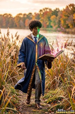 Along a grassy lake path, a young man in a blue robe carries an open magic book