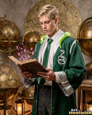 A blond man reads a spellbook with a green snake around his neck under warm room light