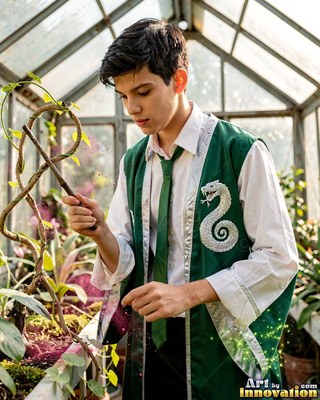 In a greenhouse, a young man dressed in a green vest points a wand at climbing vines