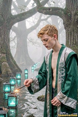 A young man wearing an unbuttoned green robe holds a small sparkler over foggy water