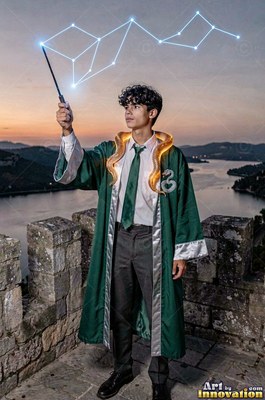 Wearing a green wizard robe, a young man raises a wand on a stone castle tower at dusk
