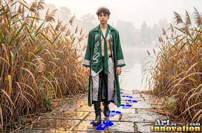 Young man in an open green coat walking past reeds by a lake
