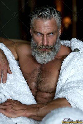 A bearded man with pale eyes looks forward wrapped in a white blanket