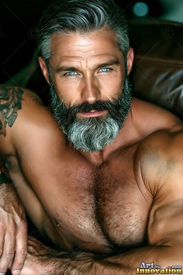 A man with a bare chest with a silver beard leans forward with bright blue eyes
