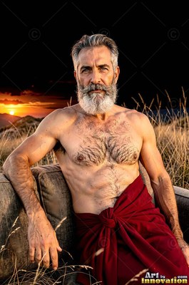 In a grassy field at sunset, a bare-chested man sporting a beard sits in a red wrap