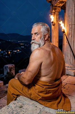 Sitting shirtless on a terrace by torches, a gray-haired man sporting a beard turns his gaze back