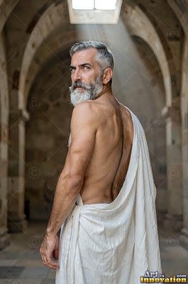 Turned back in a stone hall, a gray-bearded man wears a white toga