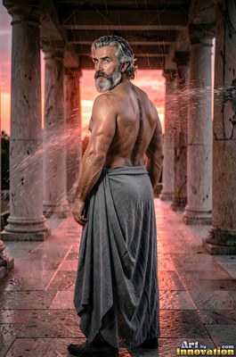 A silver-haired man looks back over his shoulder in rain by pink sunset light