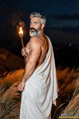 Bearded man wrapped in a white toga holding a torch outdoors at night