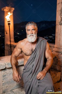 On a stone terrace at night, a muscular man with a white beard sits draped in gray cloth